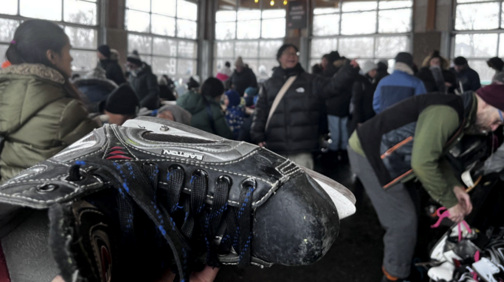 A hockey skate being held out to a large group of people inside the Assiniboine Park Duck Pond skate and skli shelter.